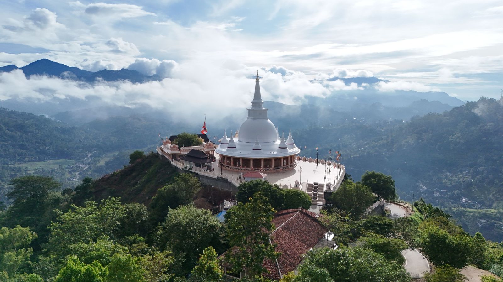 Aerial view of the monastery on its forested hilltop, with the white stupa above the surrounding hills