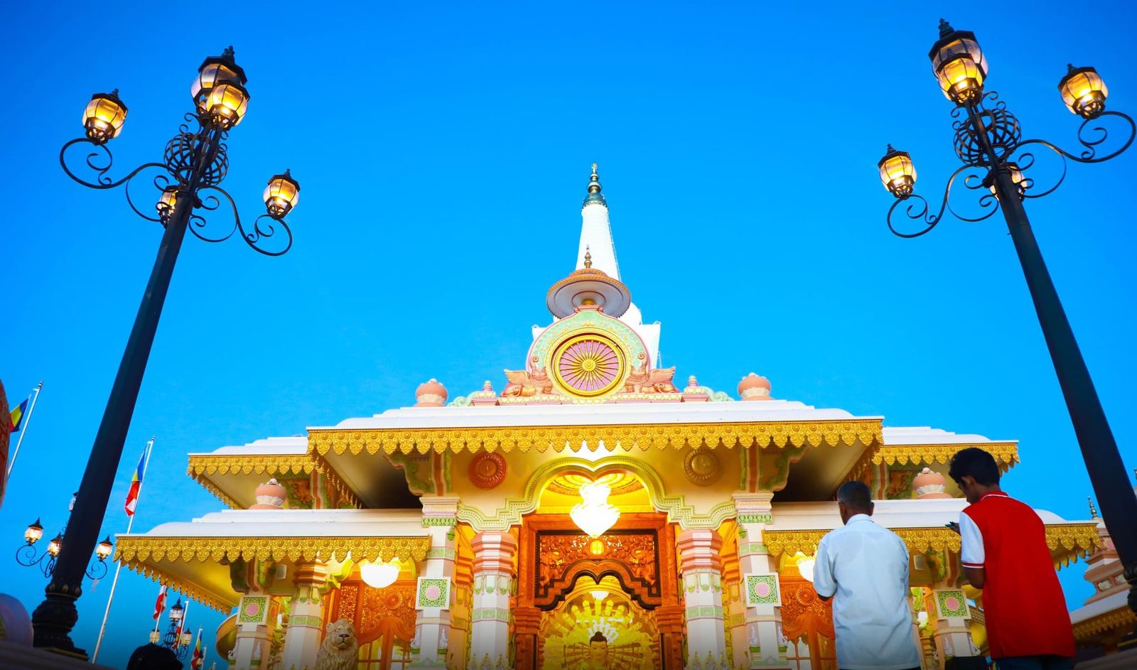 Two devotees standing before the lit, ornamented entrance at dusk