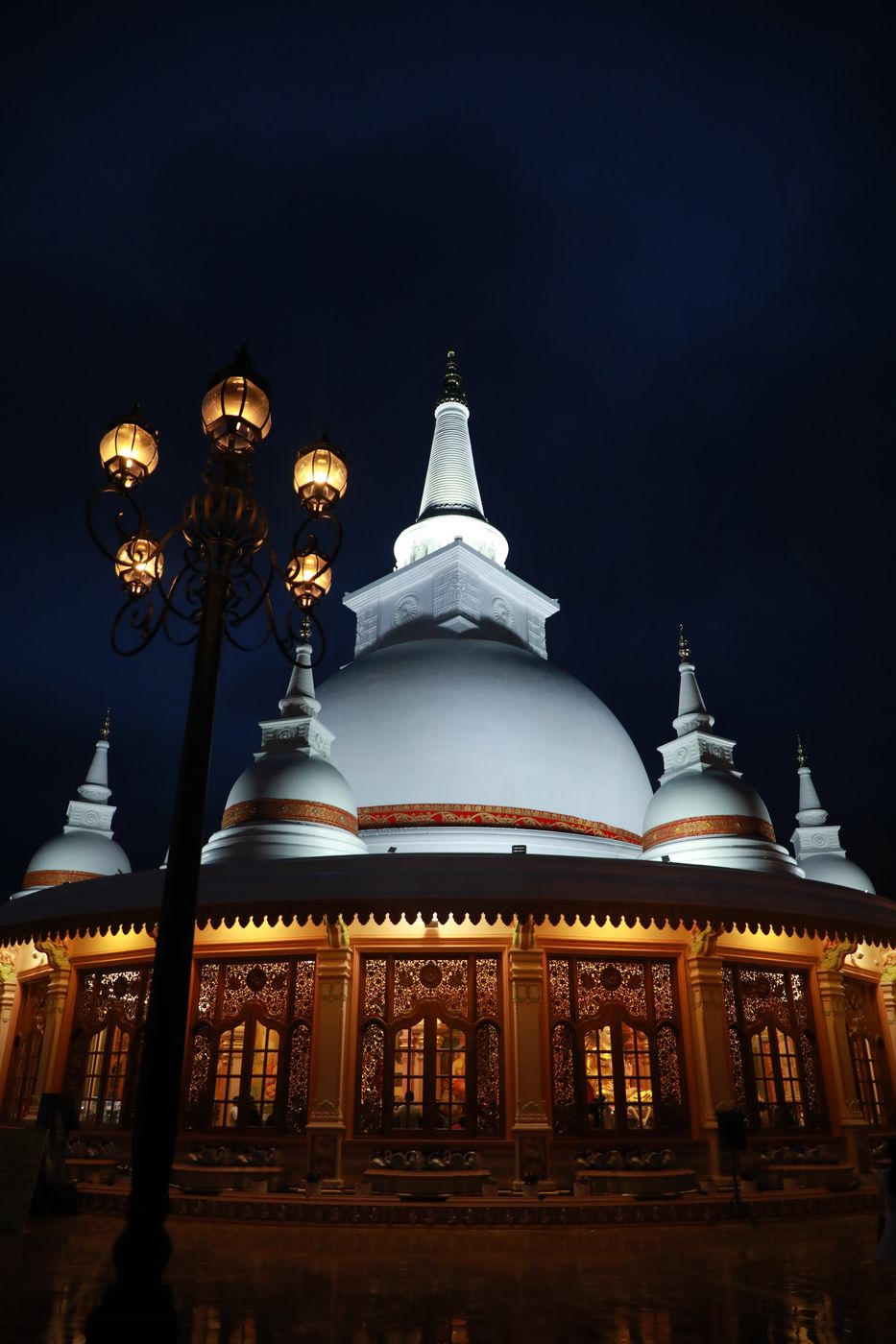 The stupa lit against a deep blue night sky beside an ornamental lamp post