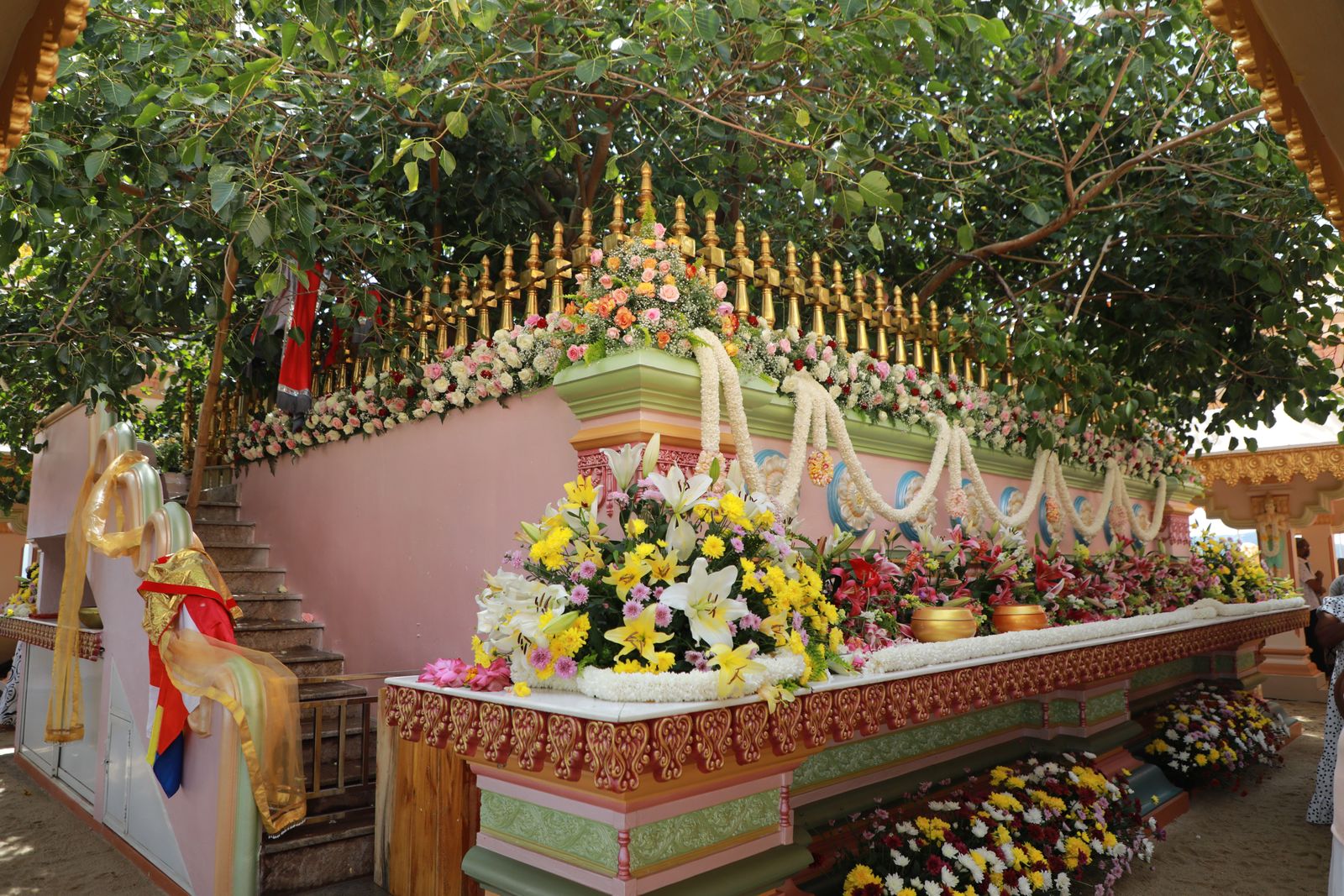 Fresh flower offerings arranged along a decorated devotional shrine beneath a spreading tree