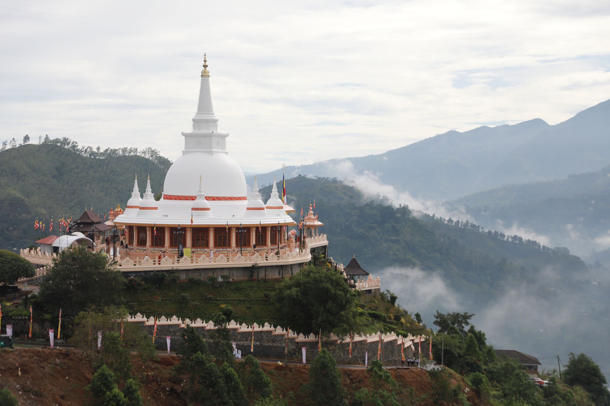The white stupa on its hilltop terrace with mountains and drifting cloud behind